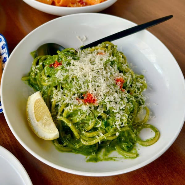 Fratelli By Jholano's vibrant green pesto pasta with grated cheese, red peppers, and a lemon wedge.