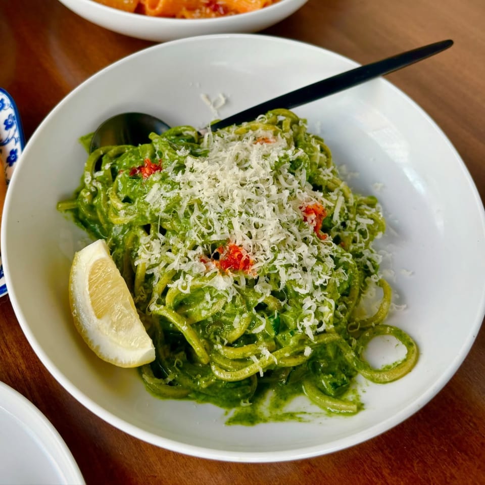 Fratelli By Jholano's vibrant green pesto pasta with grated cheese, red peppers, and a lemon wedge.