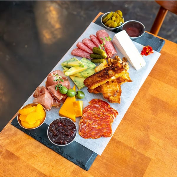 An Italian charcuterie board with various meats, cheeses, olives, pickles, and toasted bread on a wooden table.