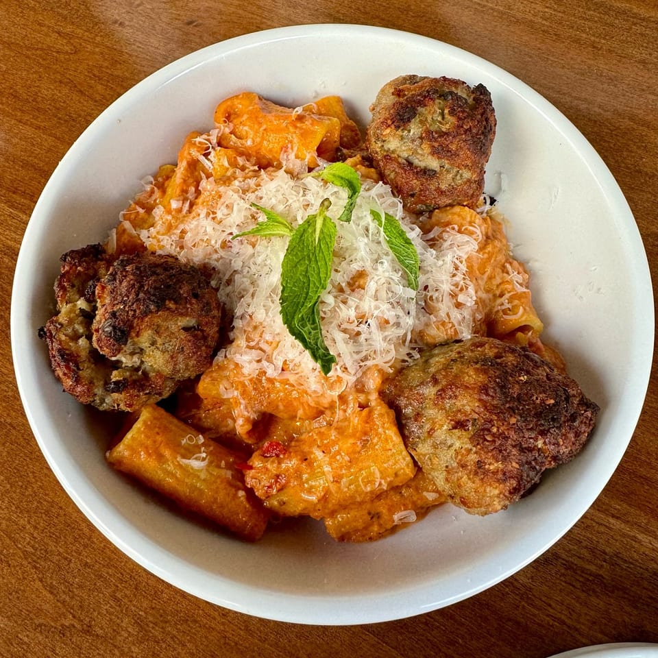 Fratelli By Jholano's rigatoni pasta with meatballs, parmesan cheese, and mint in a white bowl.