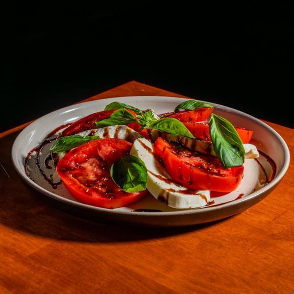 Caprese salad with sliced tomatoes, mozzarella, fresh basil, and balsamic glaze on a white plate.