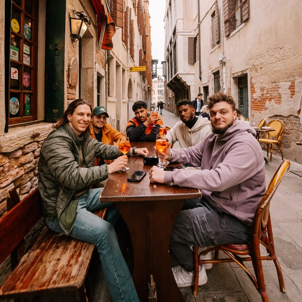 Five men enjoying drinks at an outdoor table in a narrow, historic Italian alleyway.