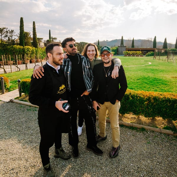 Four men, including a Fratelli By Jholano's staff member, smiling outdoors in an Italian vineyard.