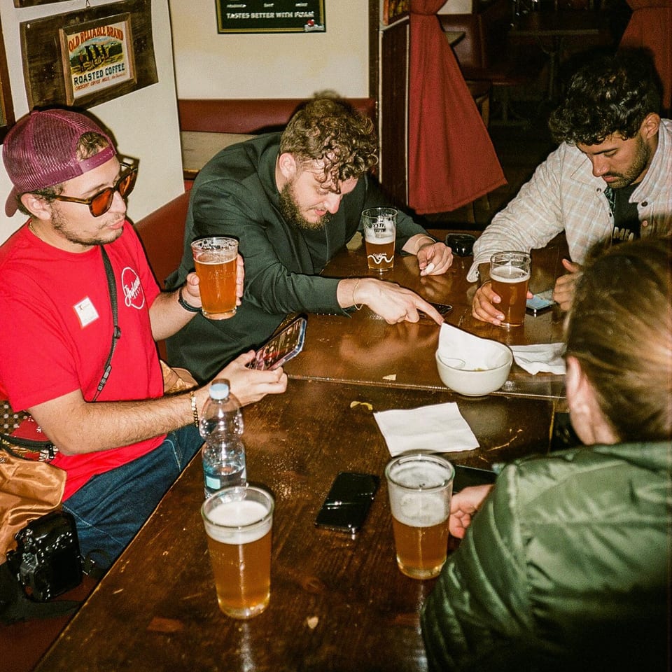 Four people gathered around a wooden table with beers and cell phones at Fratelli By Jholano's.