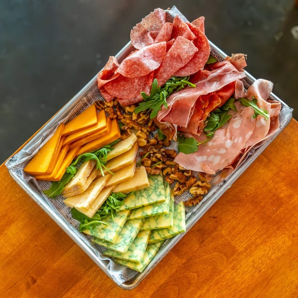 Italian charcuterie board with various cheeses, cured meats, walnuts, and arugula on a metal tray.