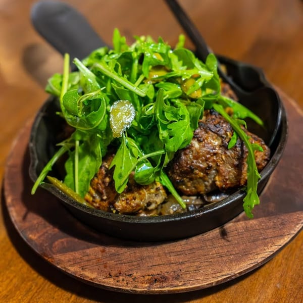 Italian meatballs topped with fresh arugula and capers, served in a cast iron skillet on a wooden board.