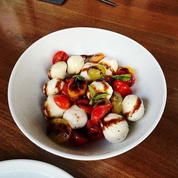 Caprese salad with mozzarella balls, cherry tomatoes, and basil, drizzled with balsamic glaze.
